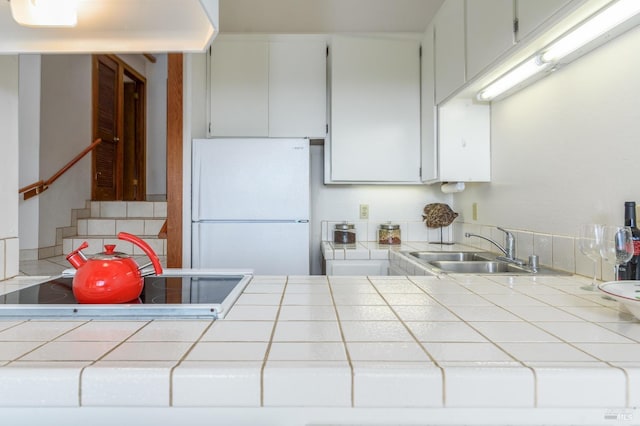 kitchen featuring tile counters, freestanding refrigerator, and a sink