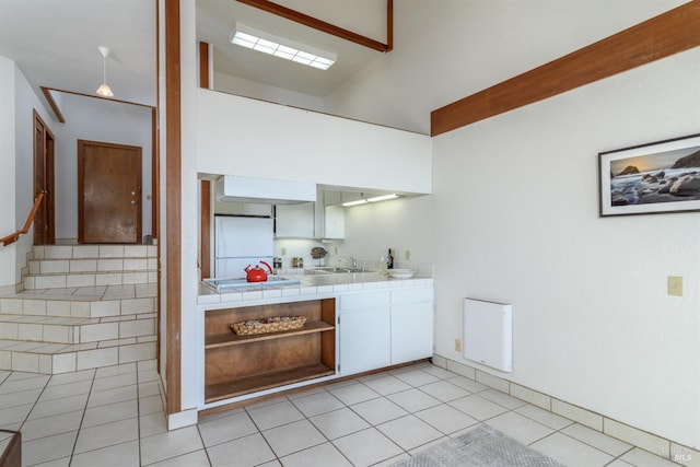 kitchen with light tile patterned flooring, a sink, tile counters, freestanding refrigerator, and open shelves