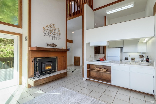 kitchen featuring tile counters, a high ceiling, light tile patterned floors, white fridge, and white cabinets