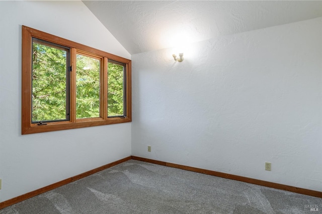 carpeted spare room featuring lofted ceiling and baseboards