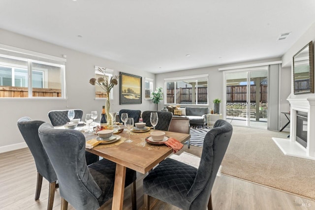 dining area featuring visible vents, wood finished floors, baseboards, and a glass covered fireplace