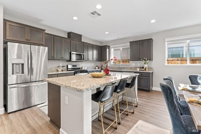 kitchen featuring a center island, light stone counters, stainless steel appliances, and light wood-style floors