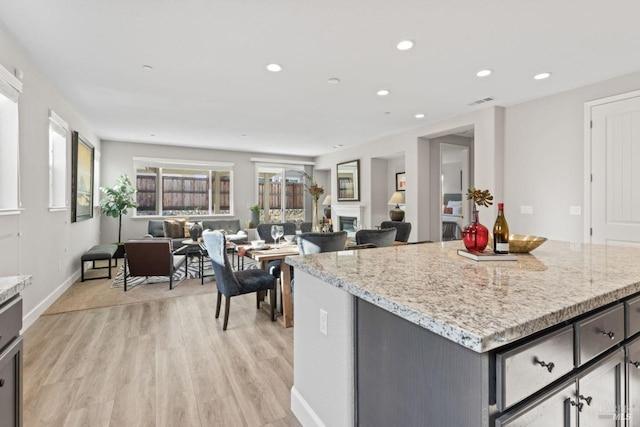 kitchen featuring light wood-type flooring, open floor plan, recessed lighting, a fireplace, and light stone countertops