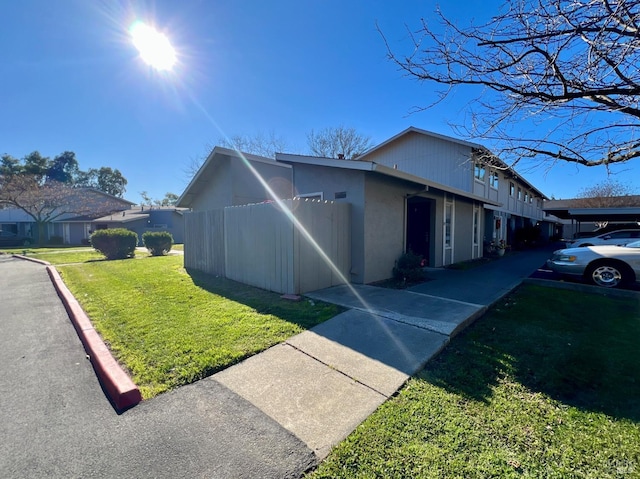 view of side of property with a lawn, fence, and stucco siding