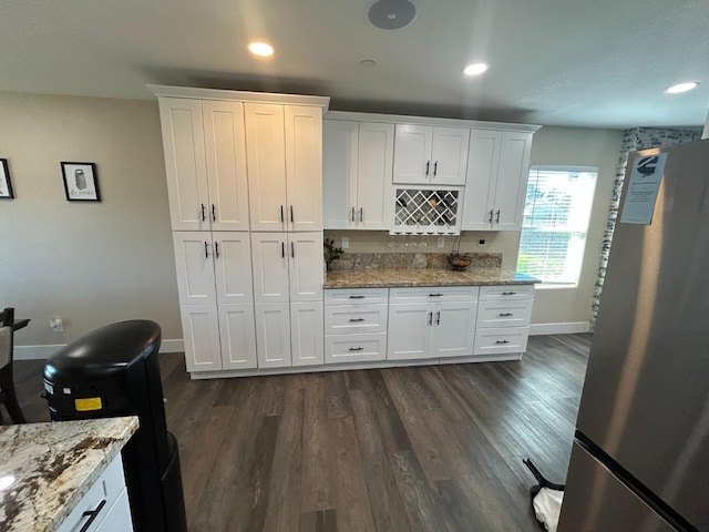 kitchen with dark hardwood / wood-style floors, light stone countertops, stainless steel refrigerator, and white cabinets