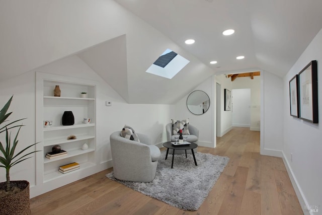 sitting room with vaulted ceiling with skylight, light hardwood / wood-style flooring, and built in shelves