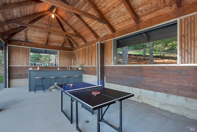 game room with wood walls, concrete floors, and vaulted ceiling with beams