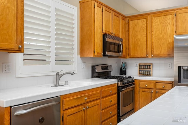 kitchen featuring sink, decorative backsplash, tile counters, and appliances with stainless steel finishes