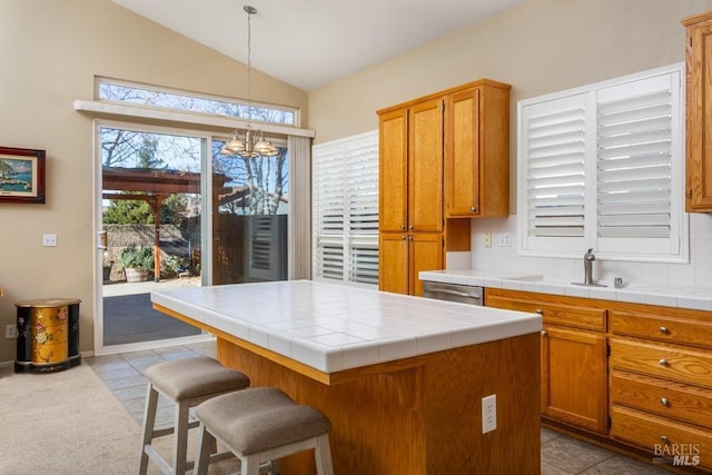 kitchen featuring tile countertops, decorative light fixtures, dishwasher, lofted ceiling, and a center island