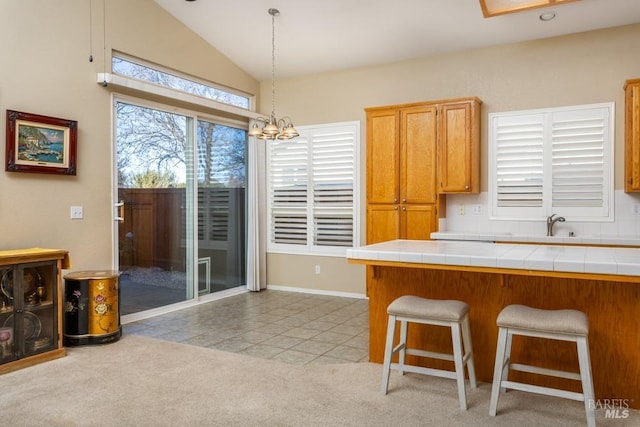 kitchen with light tile patterned flooring, a breakfast bar, pendant lighting, tile counters, and a notable chandelier