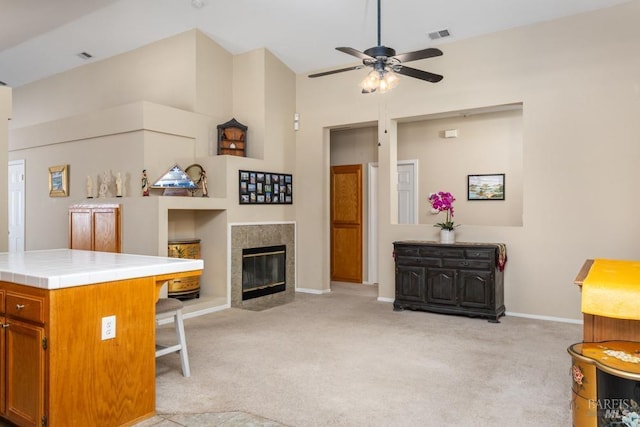 carpeted living room with ceiling fan and a tiled fireplace