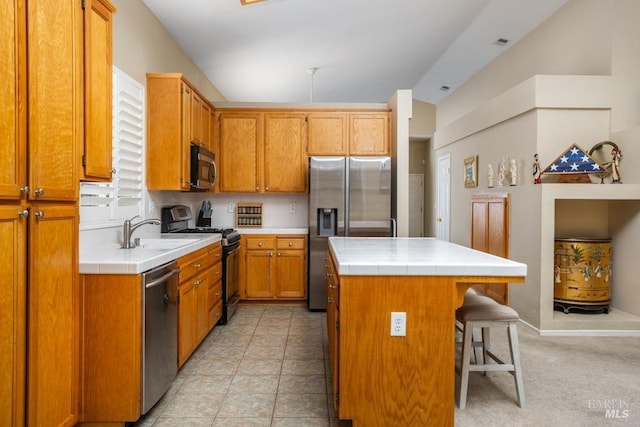 kitchen with a kitchen bar, sink, tile countertops, a kitchen island, and stainless steel appliances