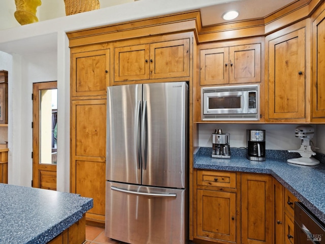 kitchen with brown cabinets, light tile patterned floors, stainless steel appliances, dark countertops, and recessed lighting