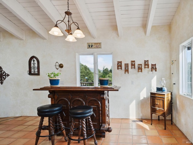 bar with hanging light fixtures, beamed ceiling, light tile patterned flooring, and a notable chandelier