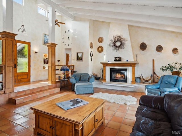 living room with a warm lit fireplace, decorative columns, a ceiling fan, high vaulted ceiling, and beam ceiling