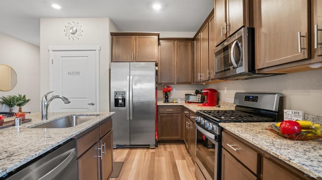 kitchen with light stone counters, light hardwood / wood-style floors, sink, and stainless steel appliances