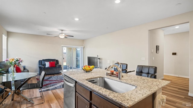 kitchen with stainless steel dishwasher, a healthy amount of sunlight, sink, light hardwood / wood-style flooring, and an island with sink