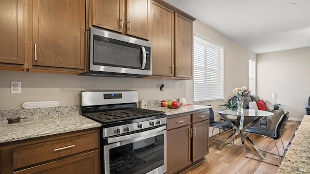 kitchen featuring appliances with stainless steel finishes, light wood-type flooring, and light stone counters