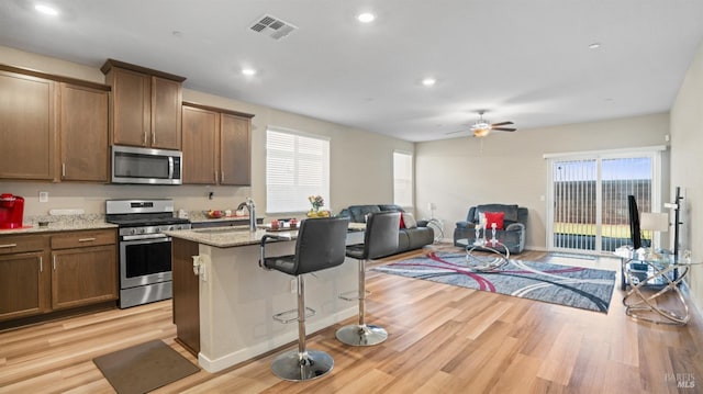 kitchen featuring sink, stainless steel appliances, light stone counters, an island with sink, and a breakfast bar