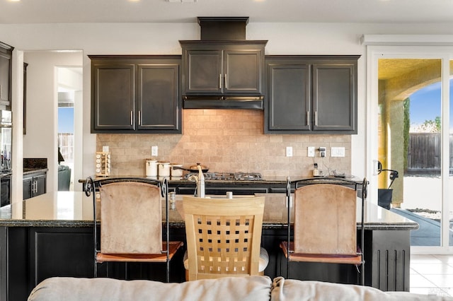 kitchen featuring dark brown cabinetry, a center island, backsplash, dark stone counters, and a breakfast bar