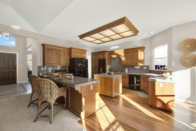 kitchen with black appliances, decorative backsplash, kitchen peninsula, and a breakfast bar