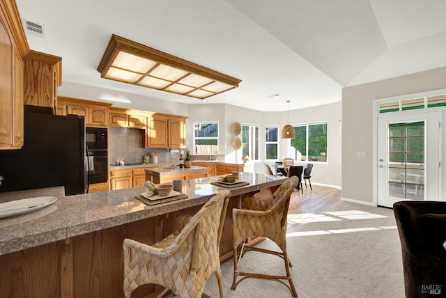 kitchen with a breakfast bar, kitchen peninsula, decorative light fixtures, light carpet, and black refrigerator