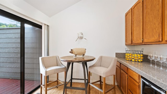 dining room featuring light hardwood / wood-style floors, vaulted ceiling, wine cooler, and bar area