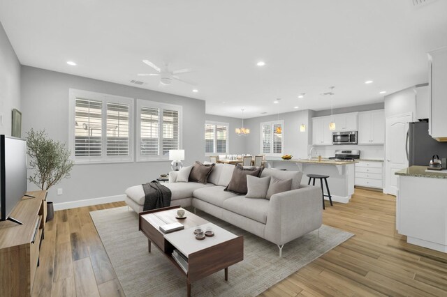 living room with light hardwood / wood-style floors, sink, and ceiling fan with notable chandelier