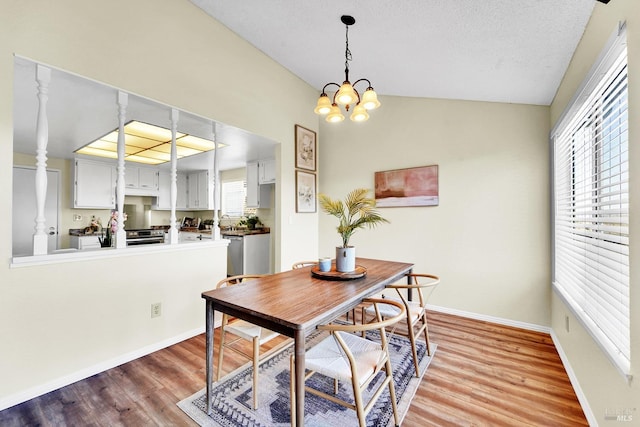 dining space with a textured ceiling, an inviting chandelier, vaulted ceiling, and light hardwood / wood-style flooring