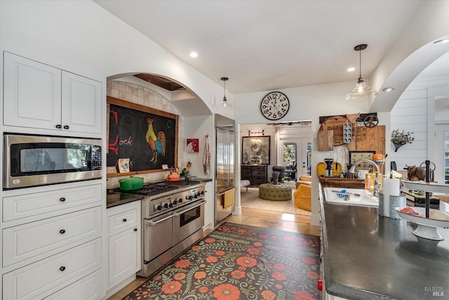 kitchen with white cabinets, dark countertops, dark wood-style floors, appliances with stainless steel finishes, and hanging light fixtures