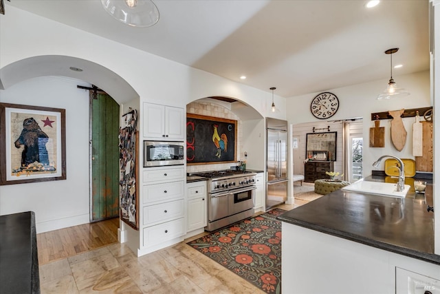 kitchen featuring white cabinets, dark countertops, built in appliances, pendant lighting, and a sink