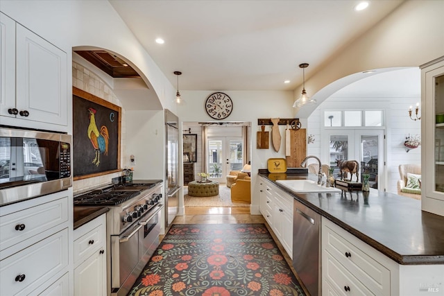 kitchen with pendant lighting, french doors, dark countertops, a sink, and built in appliances