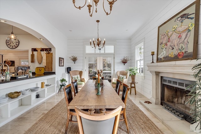 dining area featuring arched walkways, french doors, a fireplace, a notable chandelier, and wooden walls