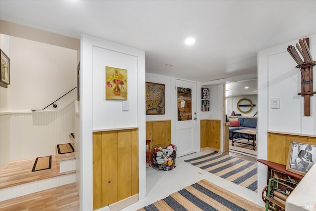 hall with light wood-type flooring and wooden walls