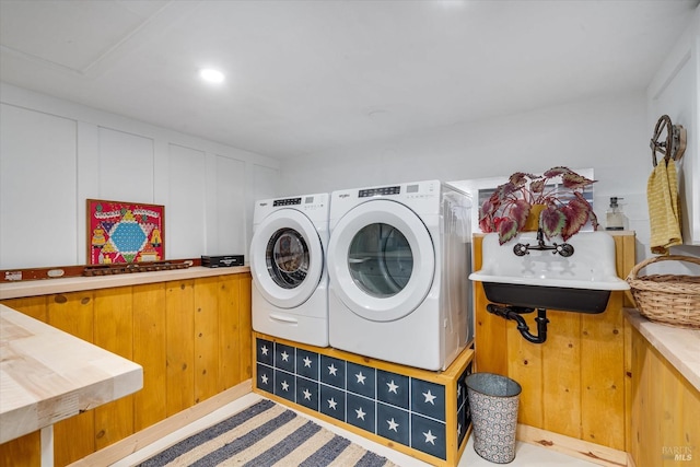 clothes washing area featuring laundry area, a decorative wall, a sink, and independent washer and dryer