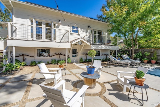 rear view of property with a balcony, a patio area, and fence