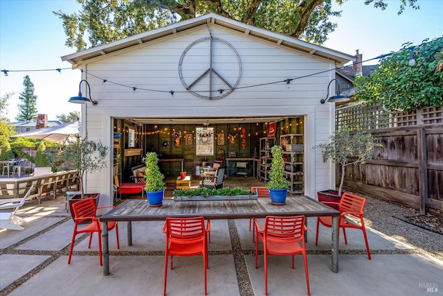 view of patio / terrace featuring outdoor dining space, a detached garage, fence, and an outbuilding