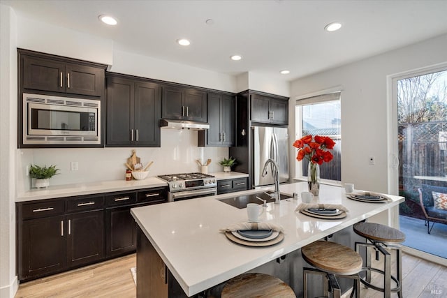 kitchen with appliances with stainless steel finishes, a kitchen breakfast bar, sink, a center island with sink, and light hardwood / wood-style floors