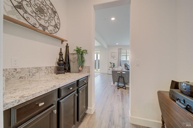 bar featuring dark brown cabinets, light stone countertops, and light wood-type flooring