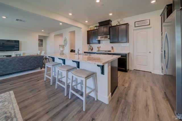 kitchen with light hardwood / wood-style flooring, a breakfast bar, stainless steel appliances, tasteful backsplash, and an island with sink