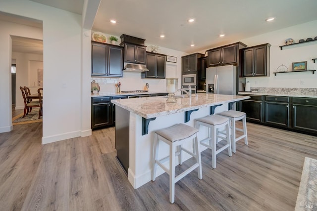 kitchen with light hardwood / wood-style flooring, a kitchen breakfast bar, an island with sink, stainless steel appliances, and decorative backsplash