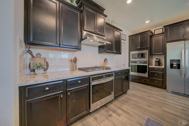 kitchen featuring dark brown cabinetry, light hardwood / wood-style flooring, appliances with stainless steel finishes, light stone countertops, and backsplash