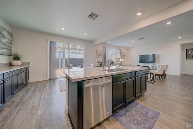 kitchen with dishwasher, sink, a kitchen island with sink, light stone counters, and light hardwood / wood-style floors