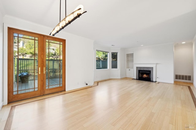 unfurnished living room featuring french doors, light hardwood / wood-style floors, crown molding, and built in shelves