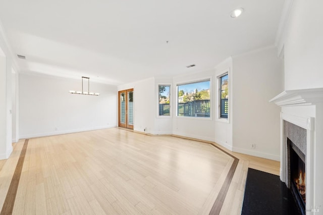 unfurnished living room with light wood finished floors, visible vents, baseboards, an inviting chandelier, and a lit fireplace