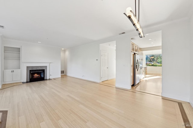 unfurnished living room featuring a lit fireplace, built in shelves, visible vents, and light wood-style floors