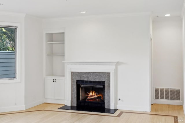 details with built in features, wood-type flooring, ornamental molding, and a tiled fireplace