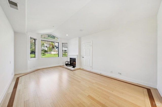 unfurnished room featuring light wood finished floors, a warm lit fireplace, visible vents, baseboards, and lofted ceiling