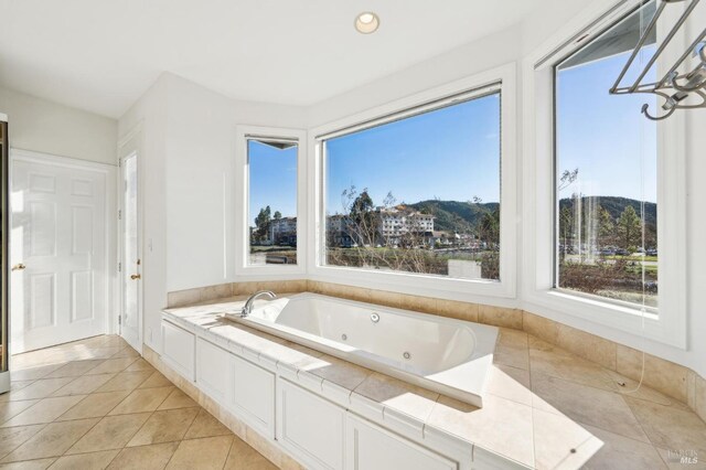 bathroom with a healthy amount of sunlight, a tub with jets, a mountain view, and tile patterned floors