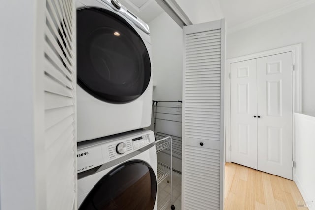 clothes washing area featuring laundry area, light wood-style flooring, crown molding, and stacked washer / dryer